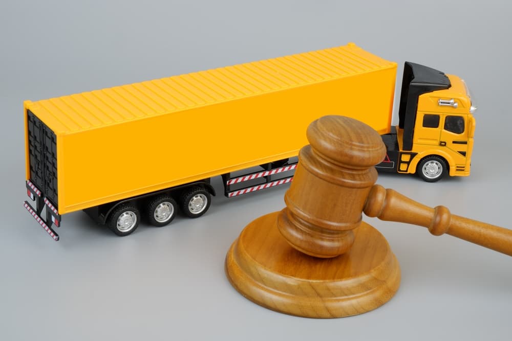 Wooden gavel and yellow cargo truck on grey background