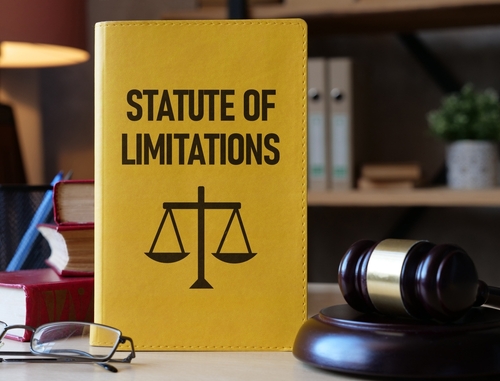 A yellow book titled "Statute of Limitations" with a scales of justice icon sits on a desk next to a gavel, emphasizing legal deadlines.