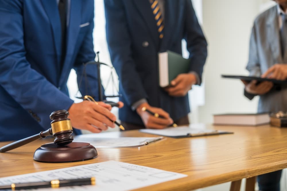 A team of business professionals and a lawyer in formal attire are seated at a desk, engaged in a discussion about a contract and legal matters.