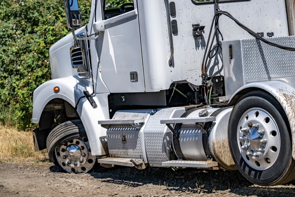 Industrial grade white big rig semi truck with a twisted wheel and a punctured tire standing out of service on the road