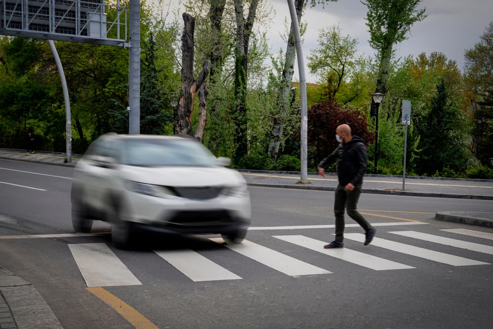 Pedestrian walking on zebra crossing and a driving car failing to stop in blurred motion.