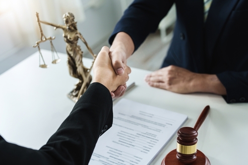 A handshake between two individuals, with legal documents, a gavel, and Lady Justice statue on the table, representing an agreement in a legal consultation.