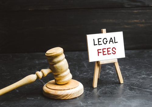 A wooden gavel placed beside a small sign that reads 'Legal Fees' on a black surface, symbolizing the costs associated with legal services.