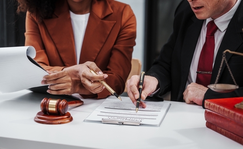 professional setting where a diverse group of individuals, possibly lawyers and clients, are engaged in signing a document. This scene is likely in a law office, as suggested by the presence of legal books and the scales of justice, underscoring the formal legal processes involved.