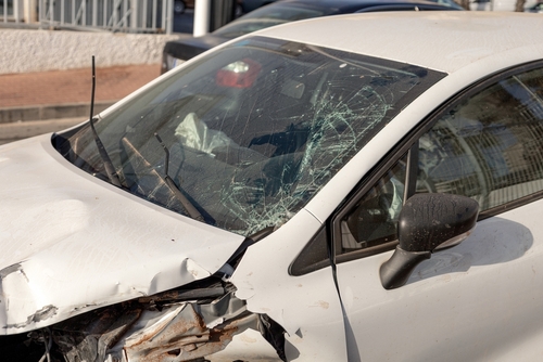 A white car with significant front-end damage and a cracked windshield, indicating it was involved in a serious accident.