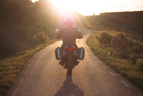 A motorcyclist riding along a peaceful road at sunset, symbolizing the freedom of riding with safety precautions in place.