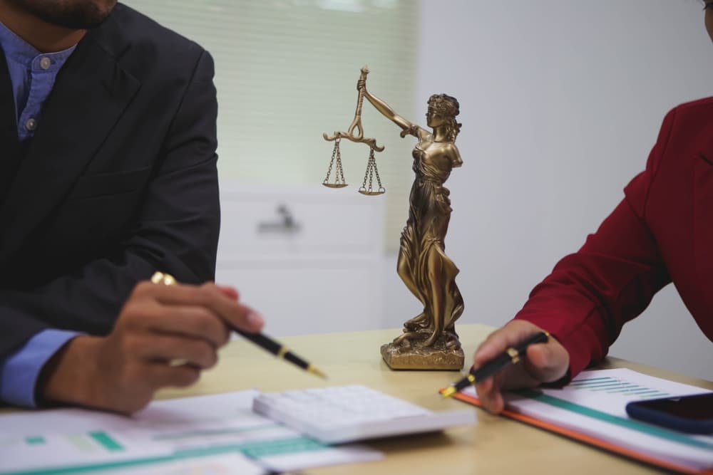 Two lawyers discussing a case with a Lady Justice statue on the table between them.