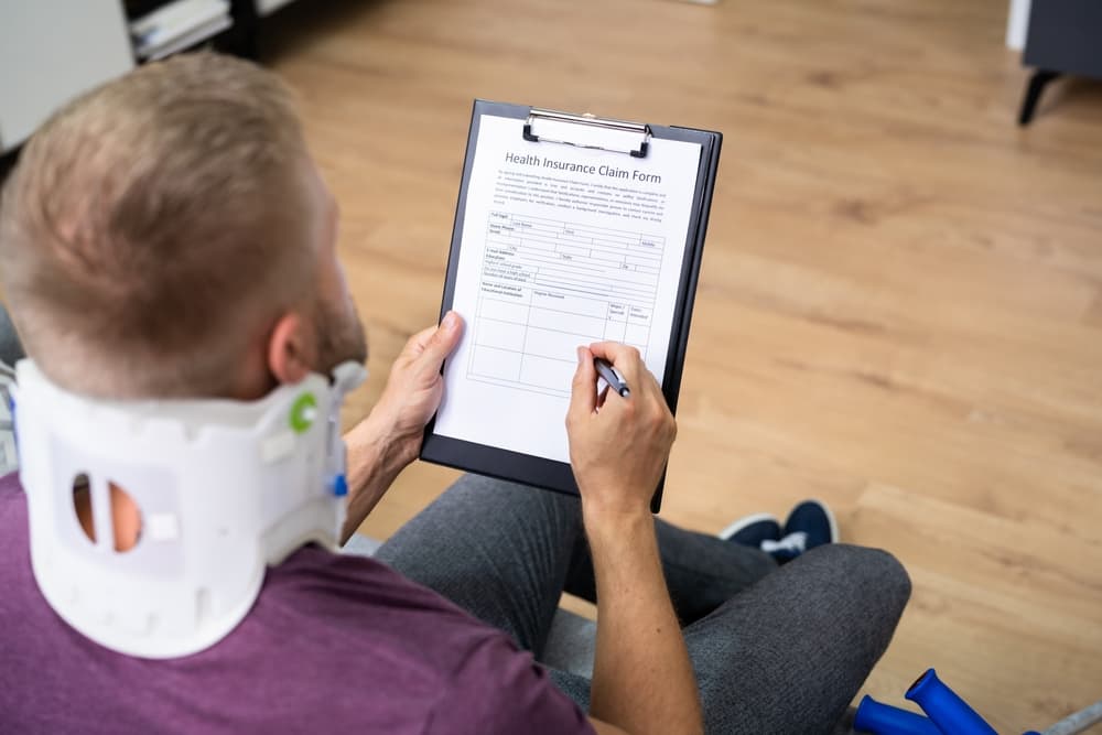 A person wearing a neck brace signing an injury claim form.