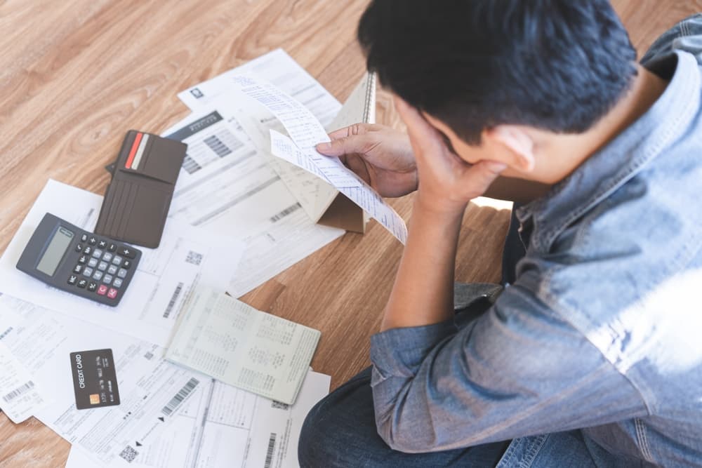 A financial concept showing a young man sitting, feeling stressed and confused while calculating expenses from an invoice and credit card bill, with no money to pay his mortgage.