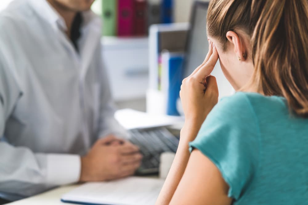 A woman experiencing a severe head and brain trauma seeks medical attention during a doctor’s appointment in an office.