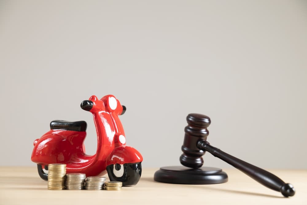 Close-up of a red motorbike piggy bank with a judge's gavel and money, set against a free background with copy space.