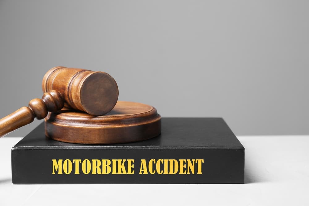 Motorbike accident law book and a judge's gavel placed on a light table against a gray background, with space for text.