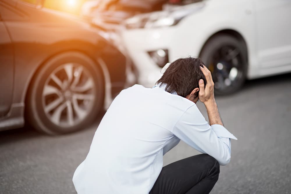 A rear-end collision involving two cars on the roadside, with a man experiencing head pain, possibly indicating a traumatic brain injury.