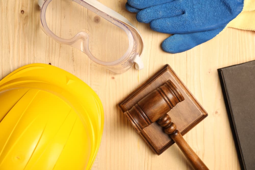 Workplace accident concept: A gavel, legal book, and protective gear arranged on a wooden table in a flat lay composition.