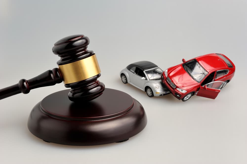 A judge's gavel rests beside models of a car accident, set against a gray background.






