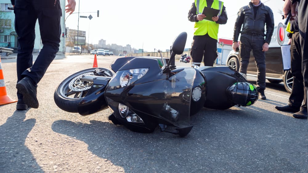 A damaged motorcycle lies on the road at the site of an accident, surrounded by scattered debris, highlighting the aftermath of a serious collision.