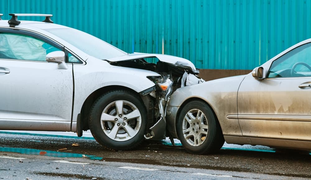 Two cars collided on the street, wrecked and blocking the road in front.