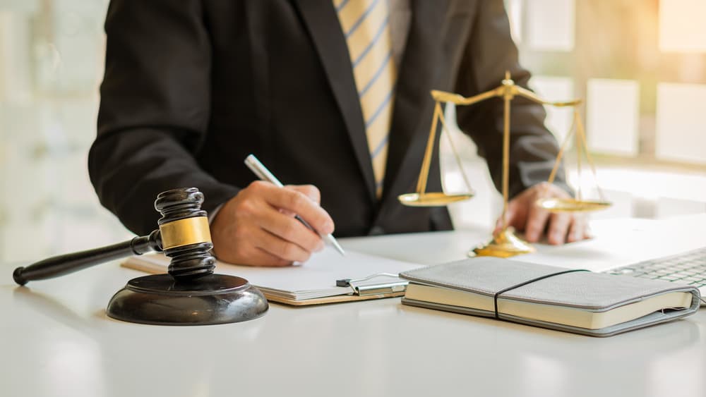 Male attorney or judge advising clients in a professional office setting, discussing legal concepts during a team meeting. A gavel and balanced scales of justice rest on the desk, symbolizing fairness and law.







