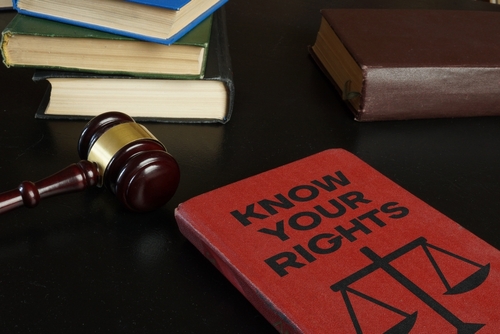 A red book titled "Know Your Rights" lies on a desk beside a gavel and stacks of legal books, symbolizing legal knowledge and justice.