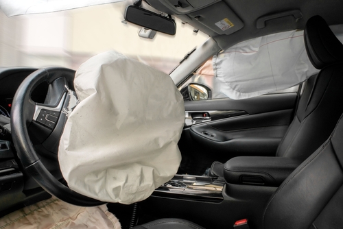 A view of a car's interior showing deployed airbags on the steering wheel and passenger side, signifying a recent collision.