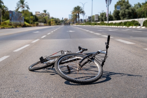 A bicycle lies on its side in the middle of an empty road, suggesting the aftermath of a possible accident.