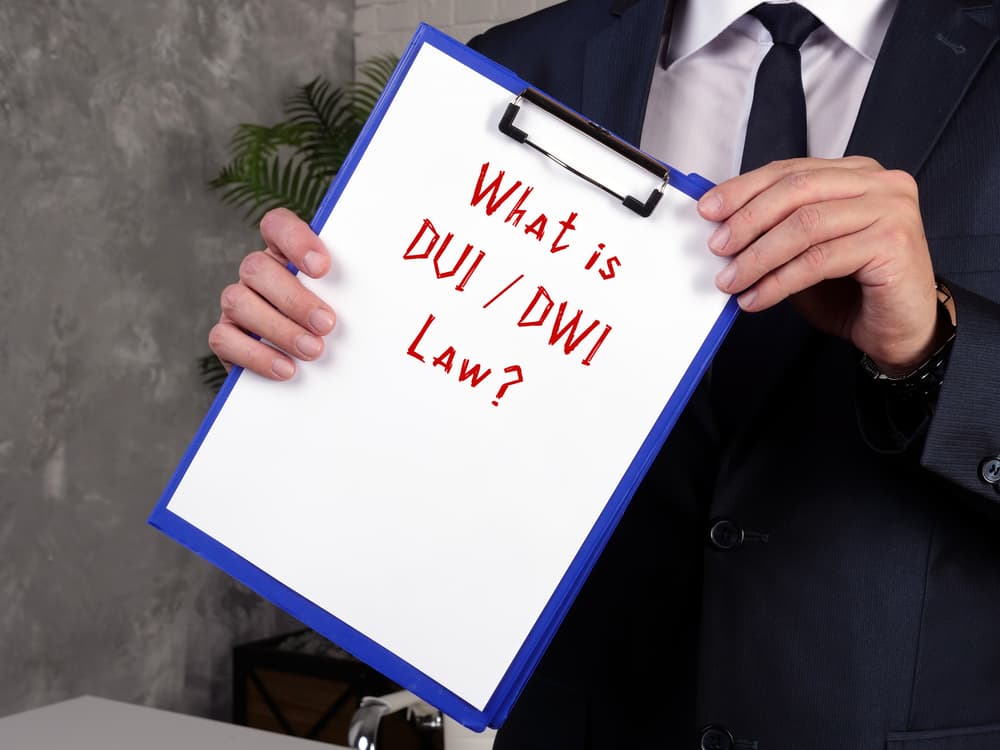 A legal representation of DUI and DWI law, featuring a judge's gavel, a glass of whiskey, and a miniature car on a desk. A piece of paper with the phrase "DUI & DWI Law" highlights the judicial concept of impaired driving regulations.