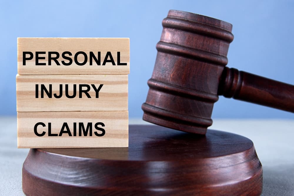 Wooden cubes spelling "PERSONAL INJURY CLAIMS" set against a background featuring a judge's gavel and stand, representing a legal business concept.