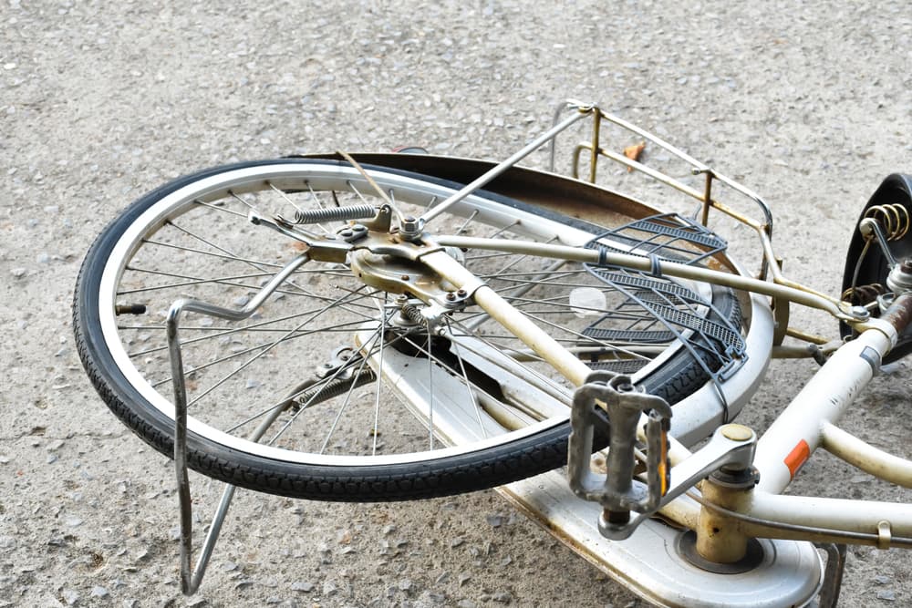 The rear wheel of the bicycle, which fell onto the cement road, is bent and deformed due to an accident and prolonged use.