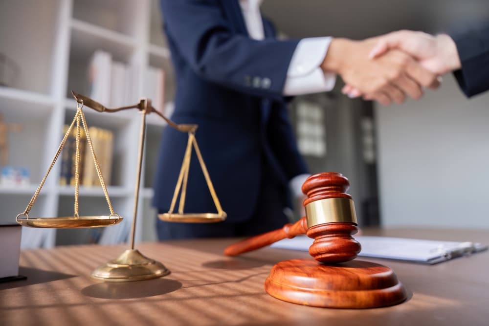 Professional lawyer handshake during a business meeting, with scales of justice and a gavel on the desk, symbolizing a successful settlement negotiation.